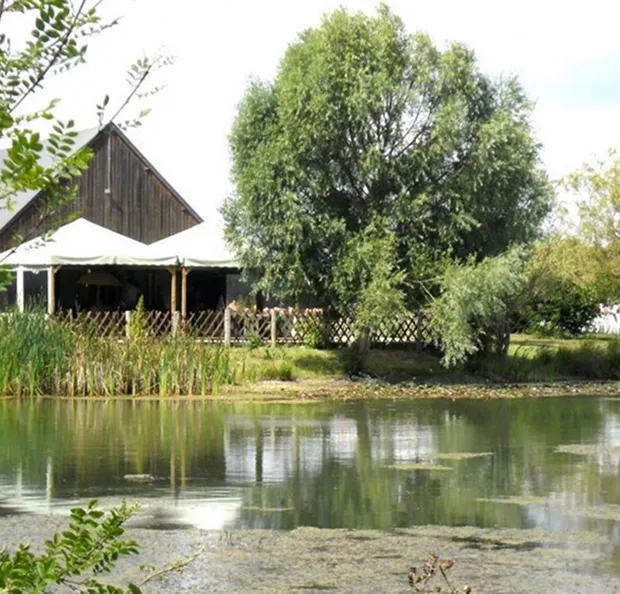 **Description pour balise alt :**
Un lac paisible reflétant des arbres et un bâtiment rustique avec une tente à Autrèche près de Tours et Amboise en Indre-et-Loire 37